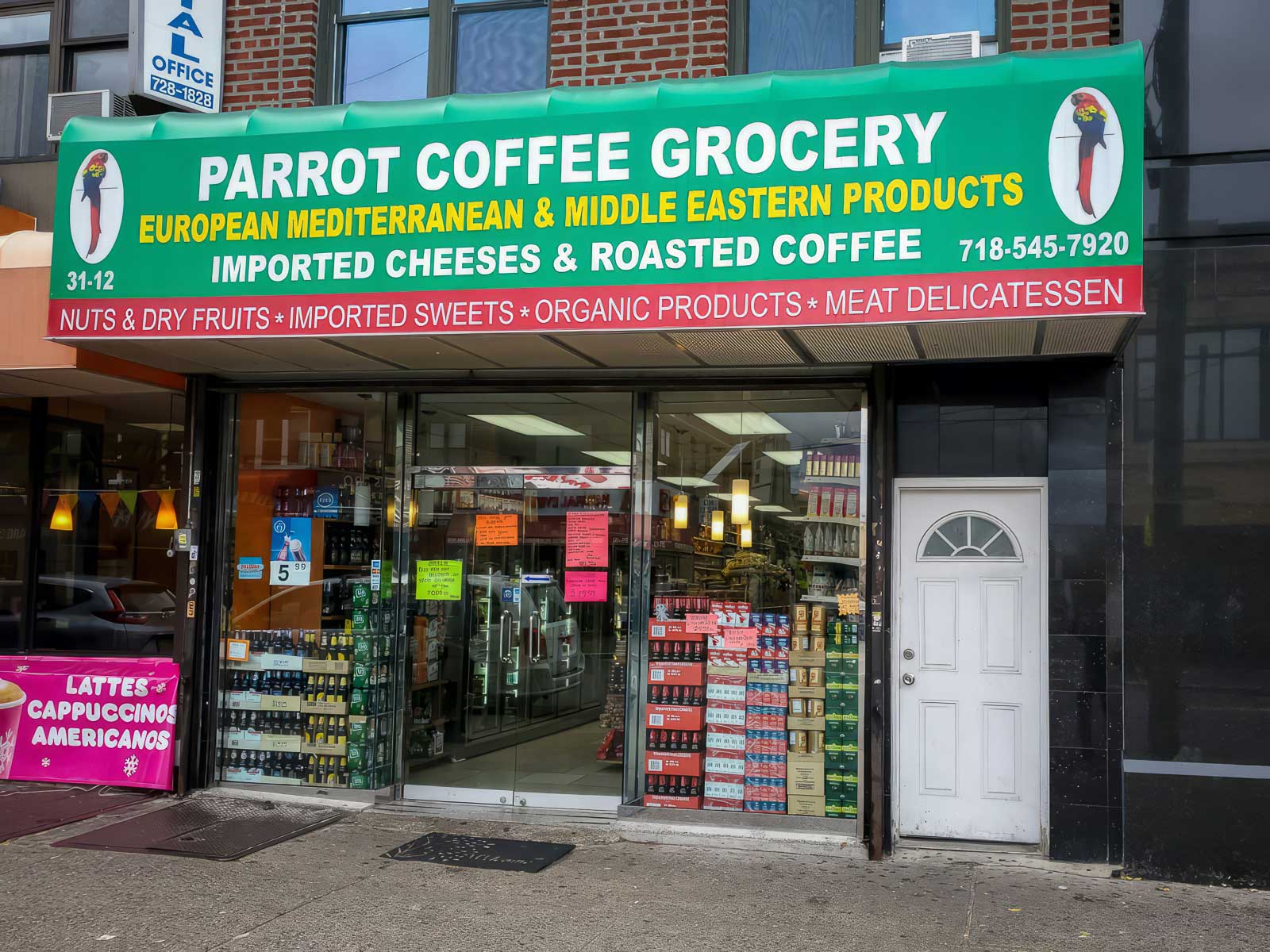 Exterior view of Parrot Coffee Grocery, featuring a green awning with the store's name, logos, and a list of offerings including European Mediterranean & Middle Eastern products, imported cheeses, roasted coffee, and other gourmet foods.