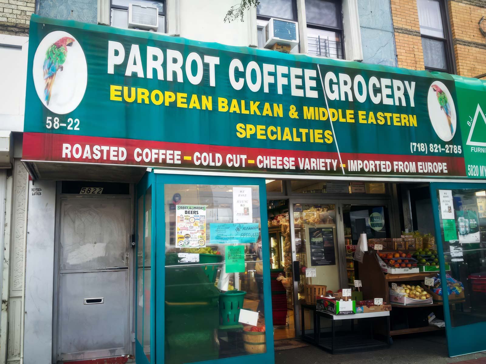 Parrot Coffee Grocery storefront with a green awning featuring the store's name, logo, and services such as European Balkan and Middle Eastern specialties, roasted coffee, cold cuts, and a variety of cheeses imported from Europe.